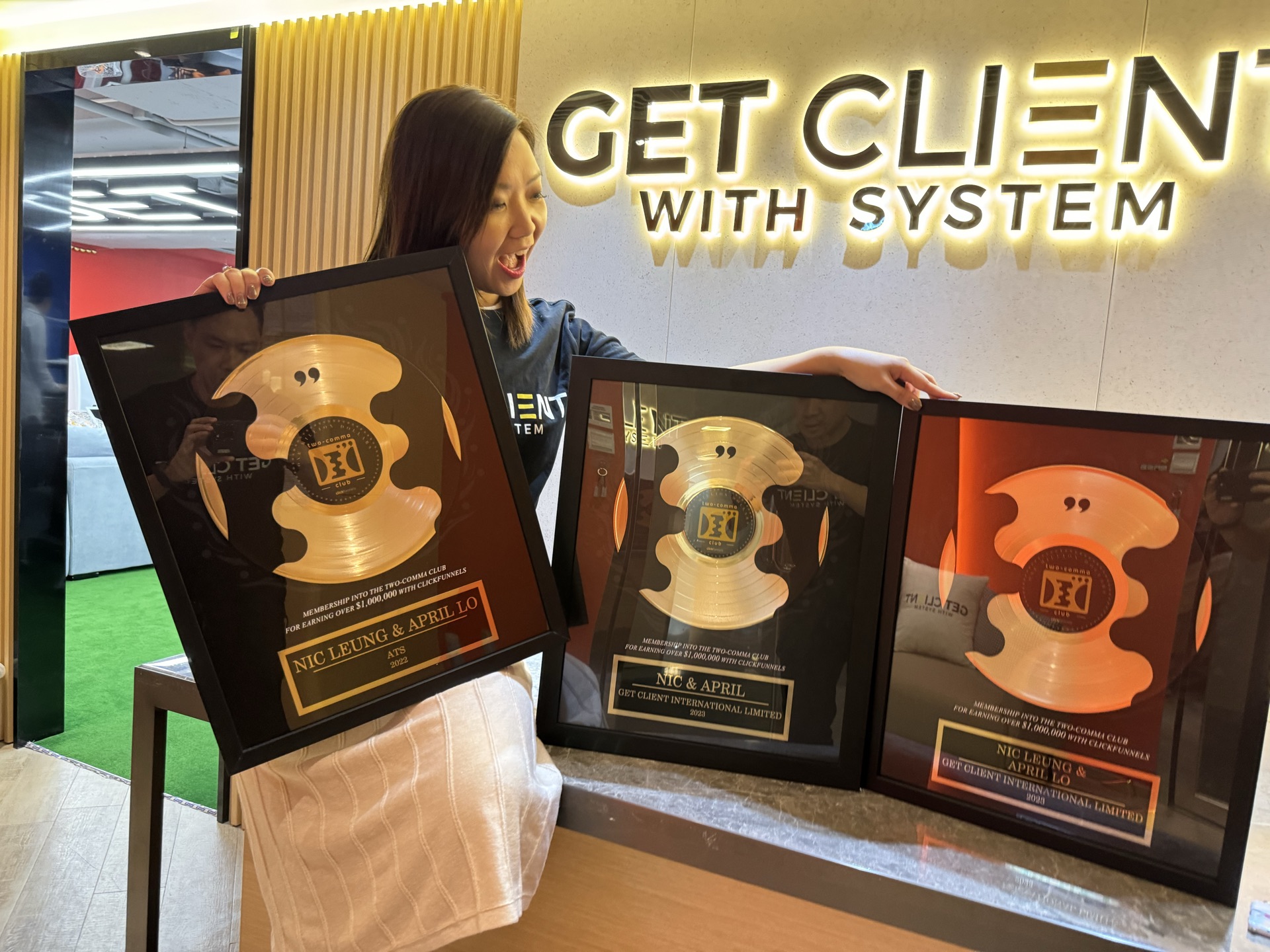 April Lo 在 GET CLIENT 招牌前抱著多座 Two Comma Club 獎座
