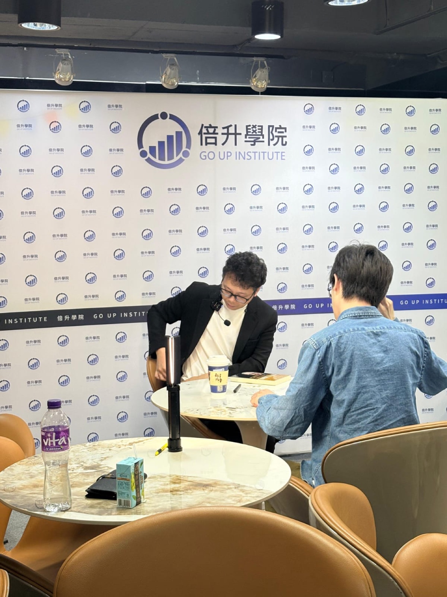 訪談式拍攝，兩位嘉賓在品牌背板前對坐